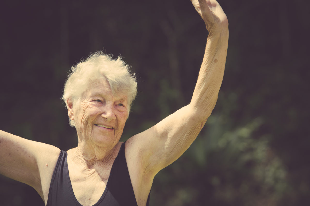An elderly woman with her hands up in an exercising position.