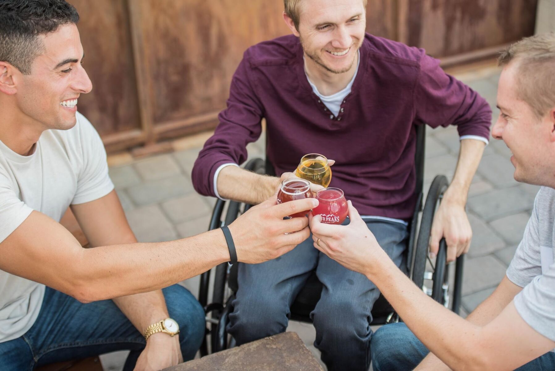 Three men say cheers with drinks. One man is in a wheelchair - Focus Care
