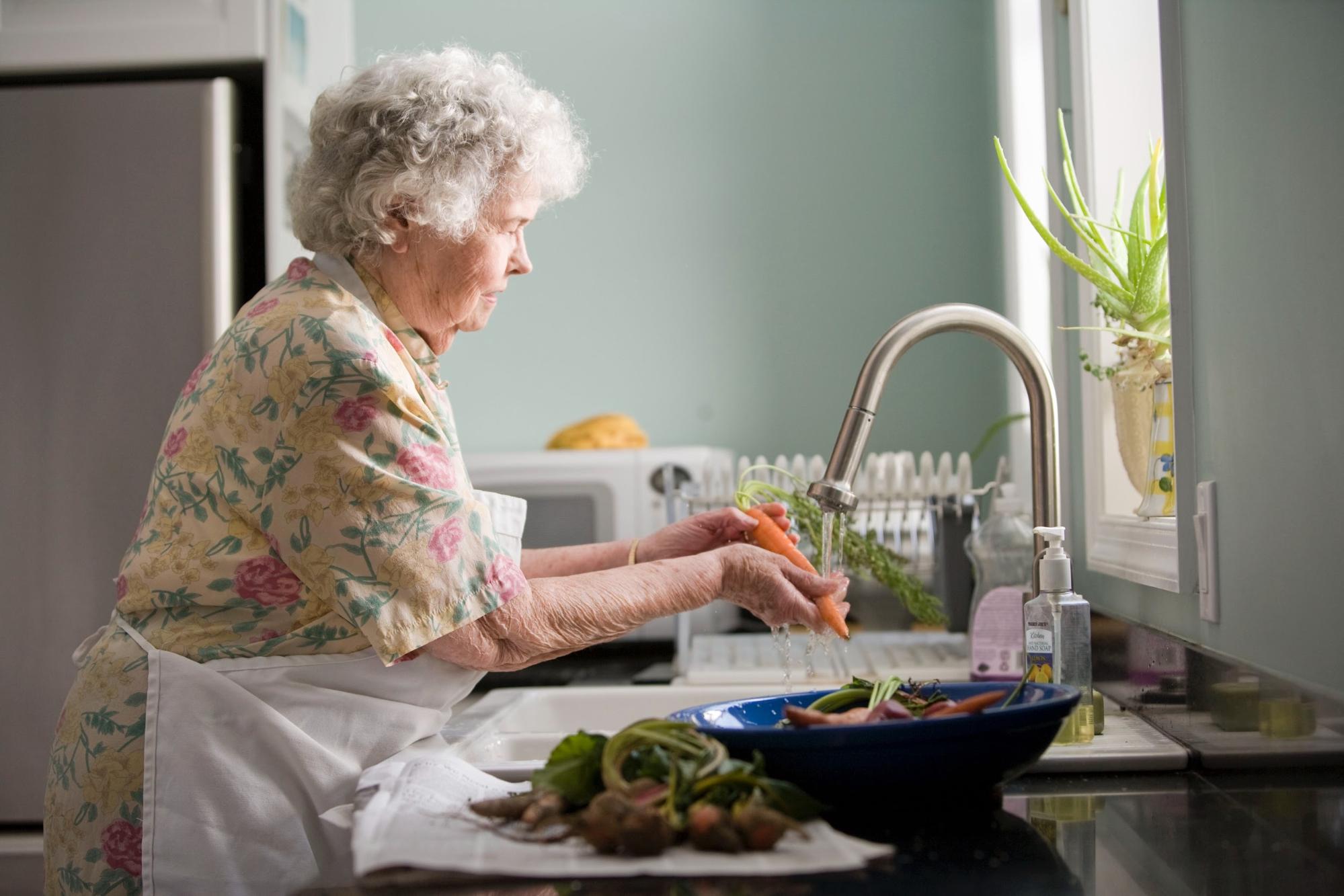 An older lady preparing vegetables in a kitchen at a sink - Dementia Caring at Home - Focus Care
