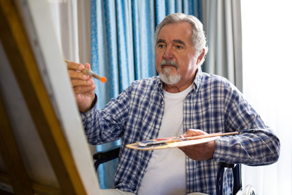 Senior man painting while sitting on wheelchair in an art therapy session