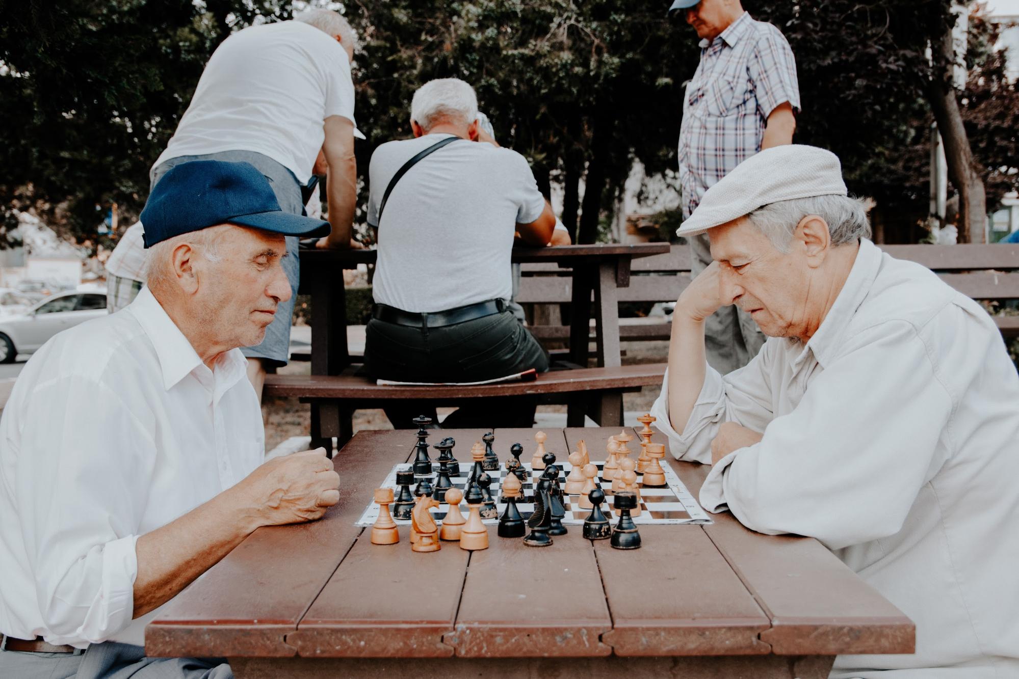 Two older men playing chess outdoors on a picnic table - Dementia Signs - Focus Care
