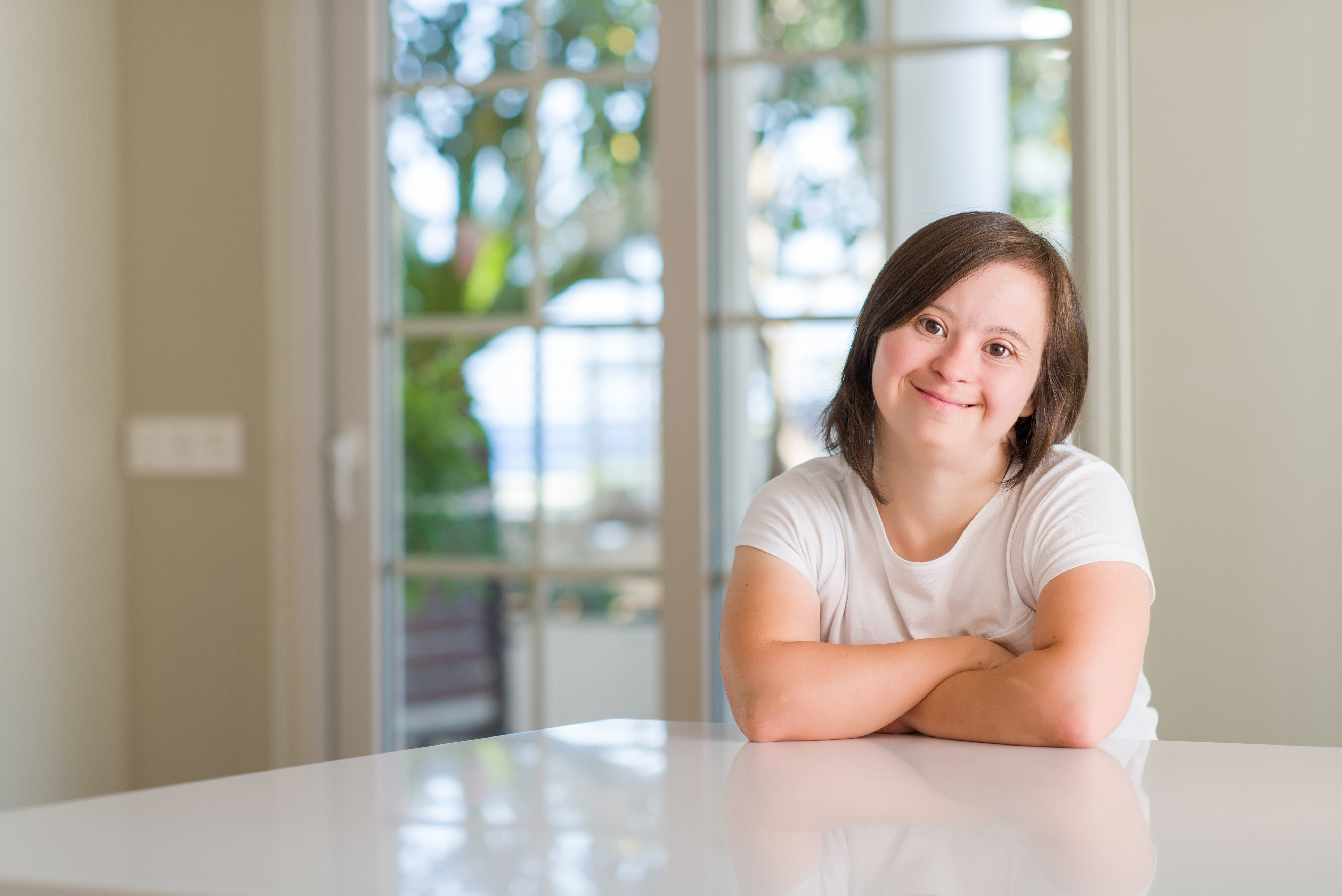 Girl in white shirt sits at table with arms folded, smiling - Call to Action - Focus Care