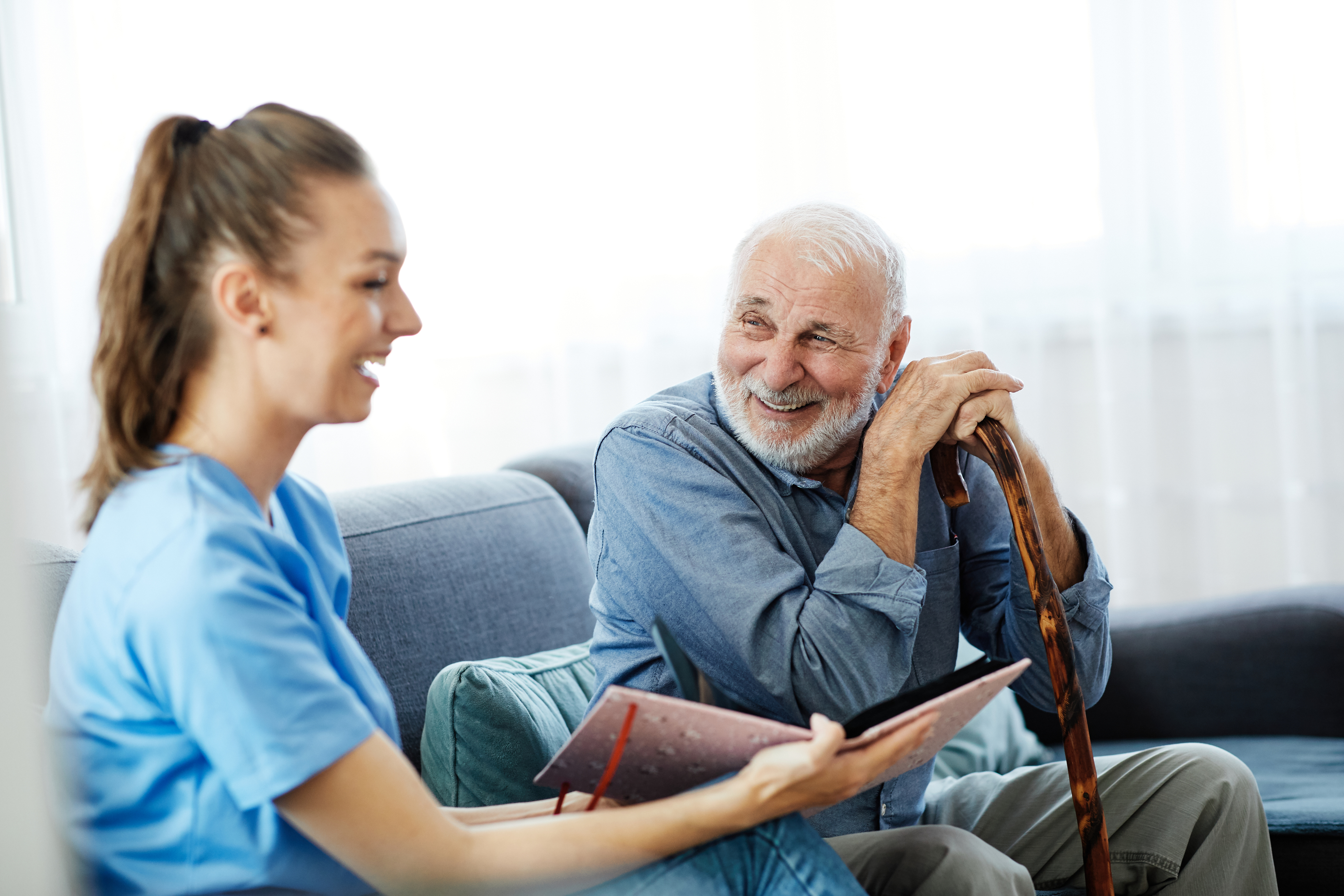 An elderly man laughs with a younger woman in Nurse scrubs - The Benefits of In-Home Nursing - Focus Care