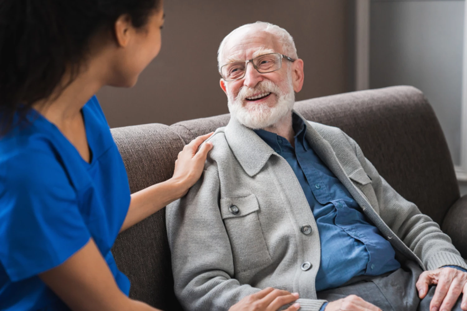 An elderly man with glasses smiling and having a pleasant conversation with a caregiver, illustrating the positive impact of personal care services on well-being.