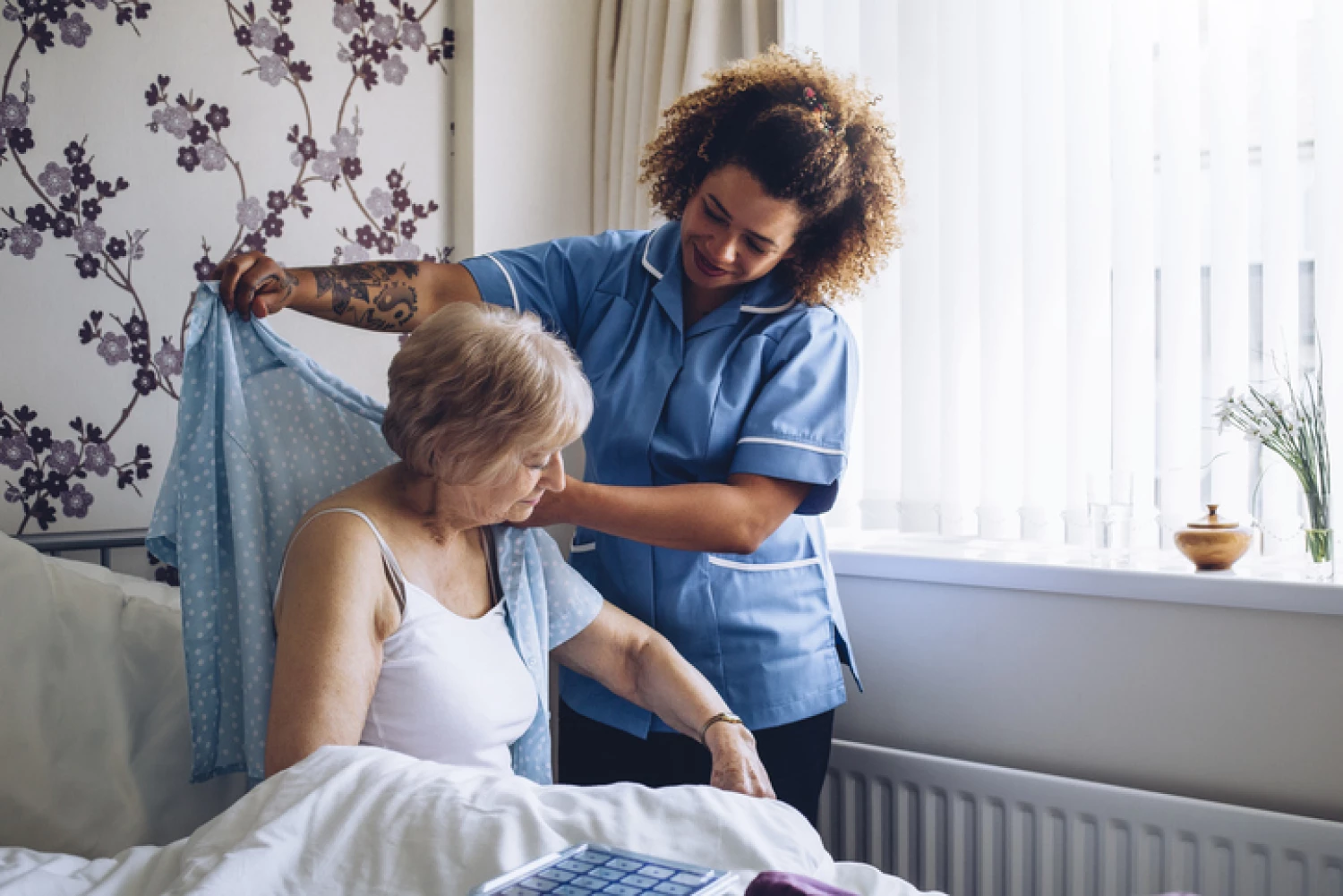 Carer assisting an elderly woman with dressing in a in-home care setting.