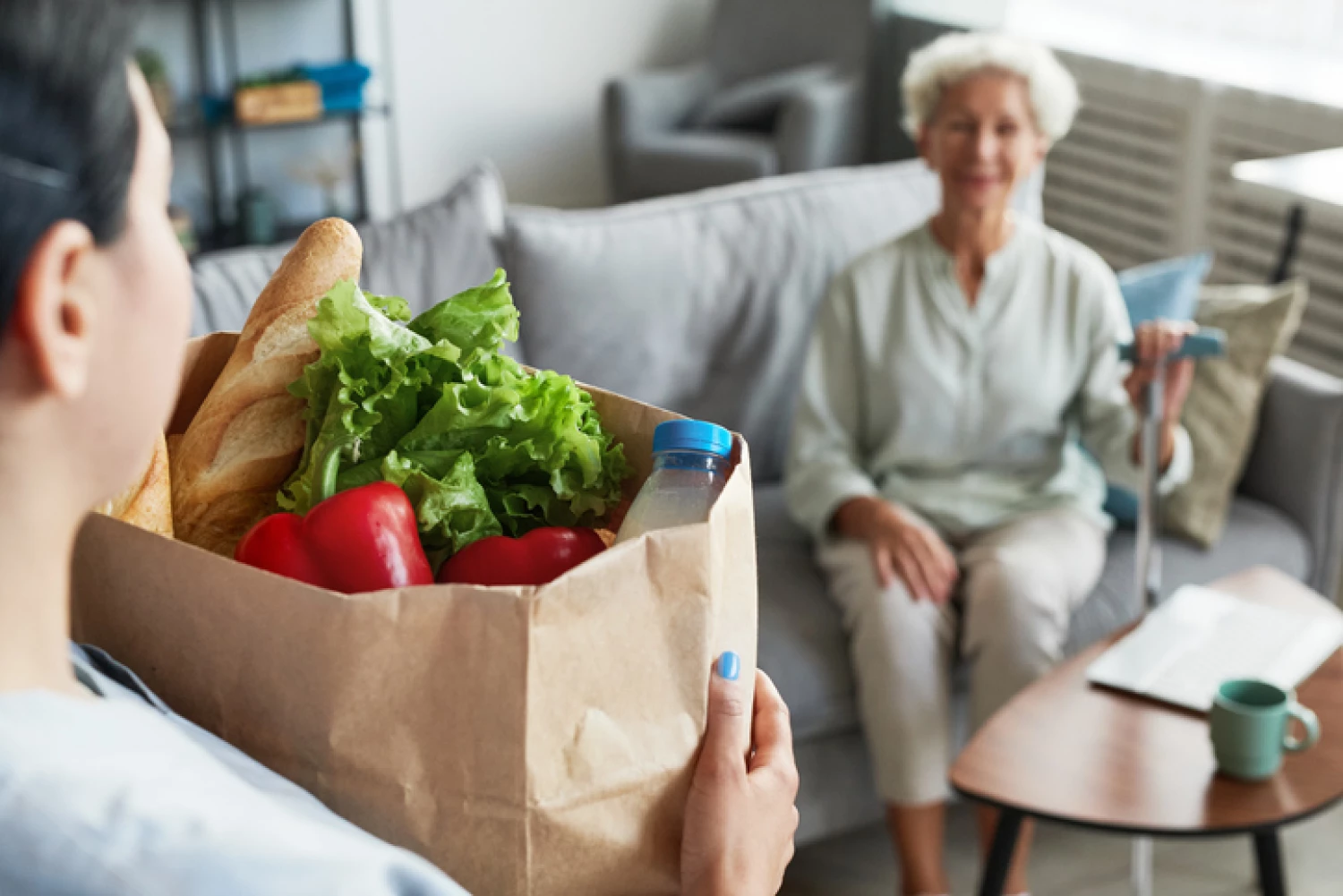 Caregiver delivering groceries to an elderly woman, showcasing support included in Home Care Package funding.