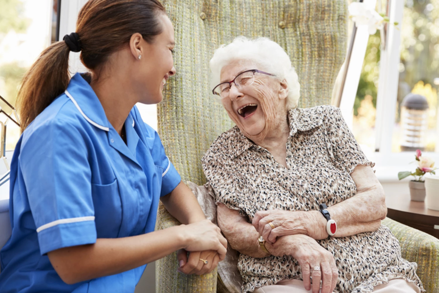 A cheerful elderly woman laughing and engaging in a friendly conversation with a nurse, highlighting the importance of companionship in personal care.