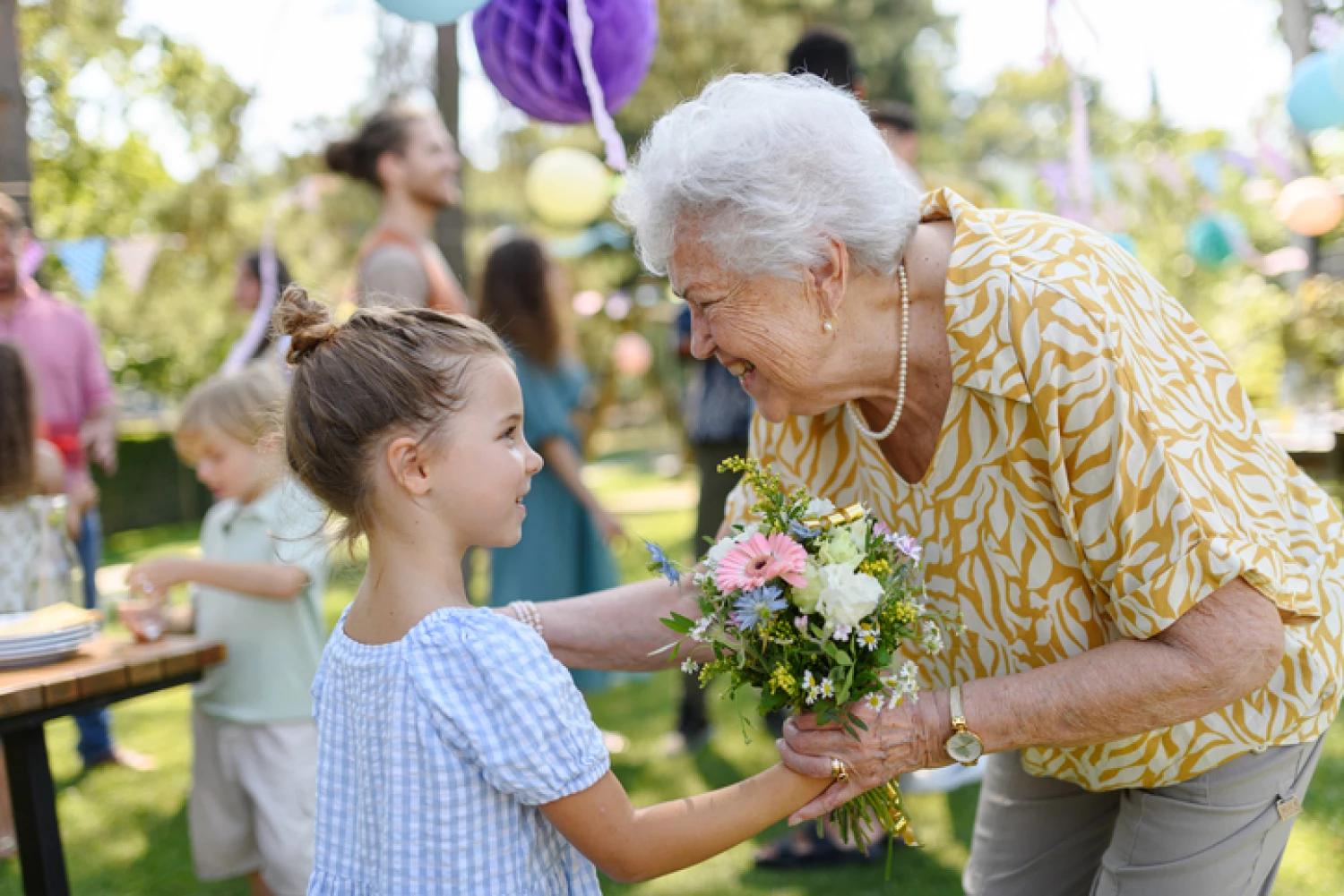 Grandmother with dementia receives flowers from a grand daughter at an outdoor gathering, symbolising the importance of family connections in dementia care.