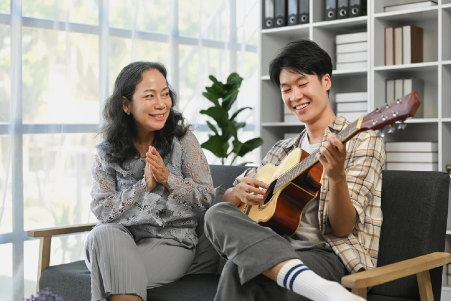 Young man plays guitar for an elderly woman, showcasing intergenerational music therapy.