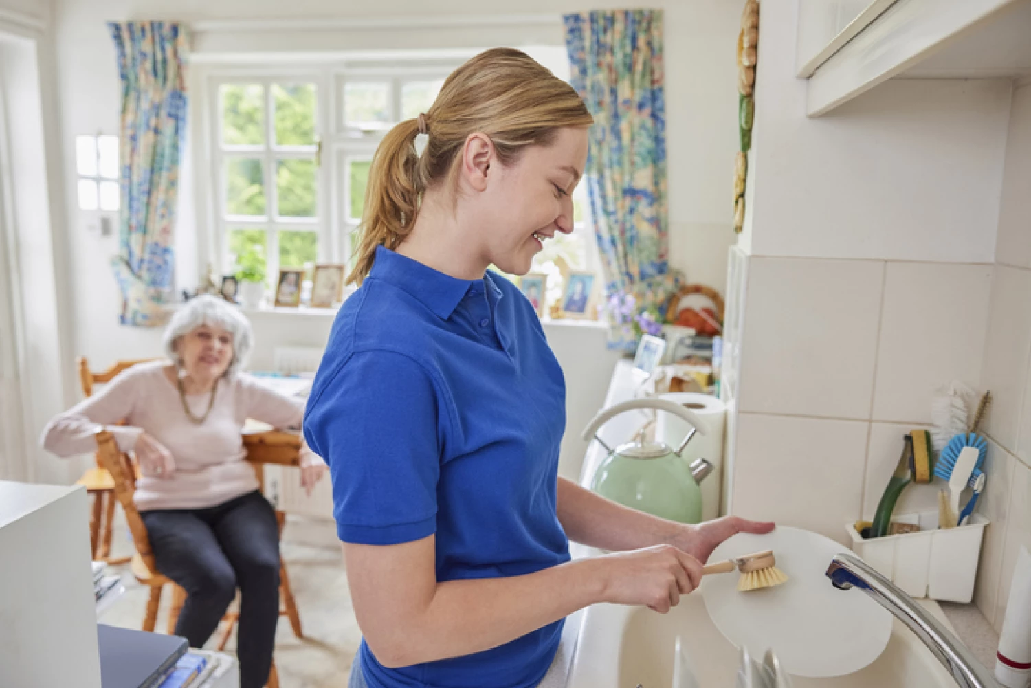 Young female caregiver assisting an elderly woman with kitchen activities, exemplifying compassionate support provided under a Level 1 home care package.