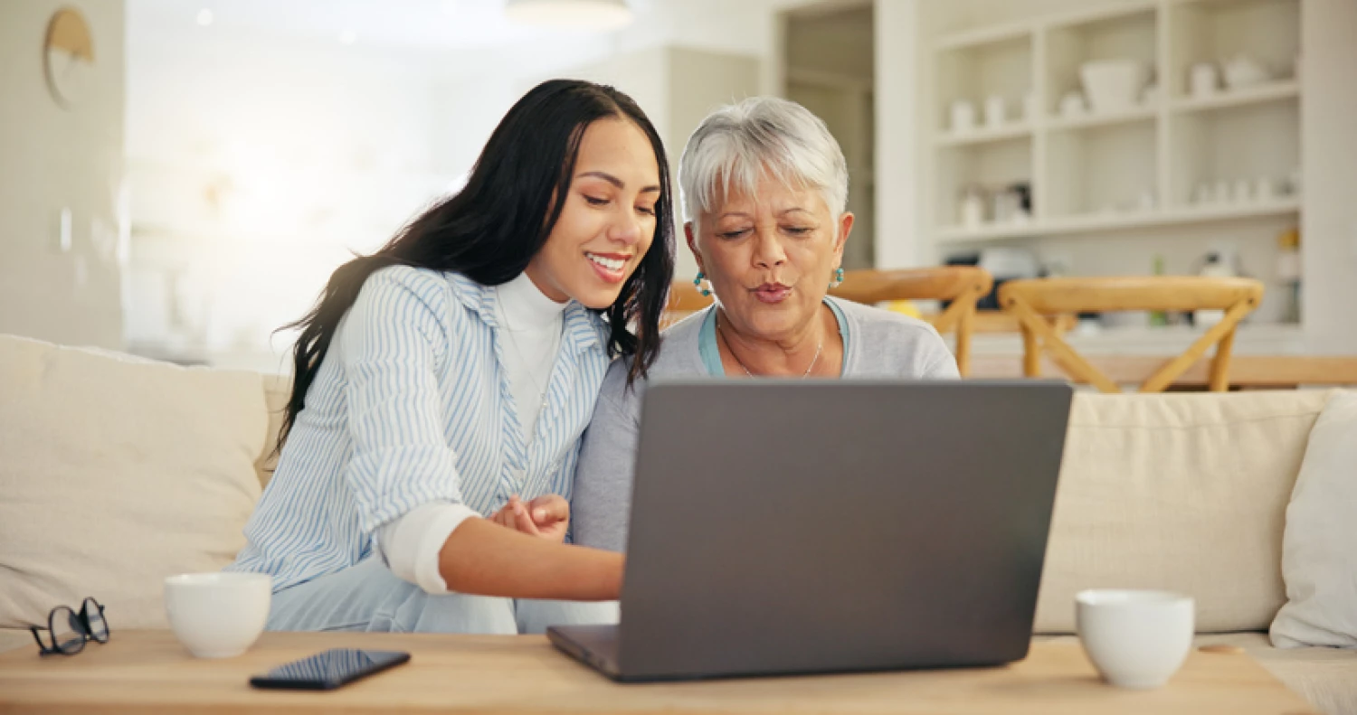 A young woman assisting an elderly mother to search for a home care provider on a laptop.
