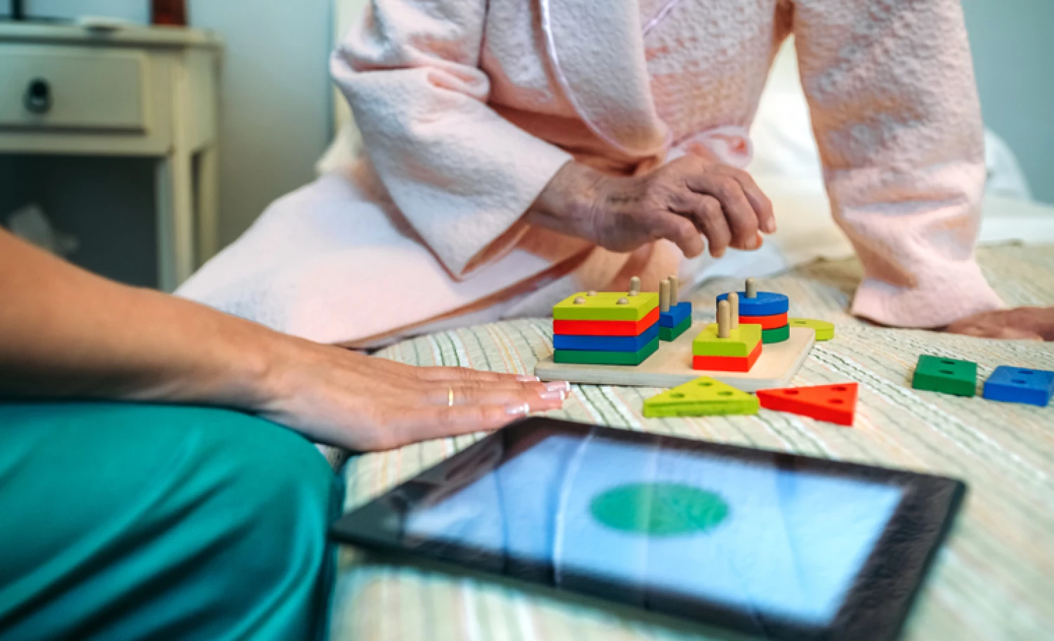 An elderly person wearing a pink robe plays with colourful geometric shapes during a Montessori session, illustrating cognitive activities for dementia patients.