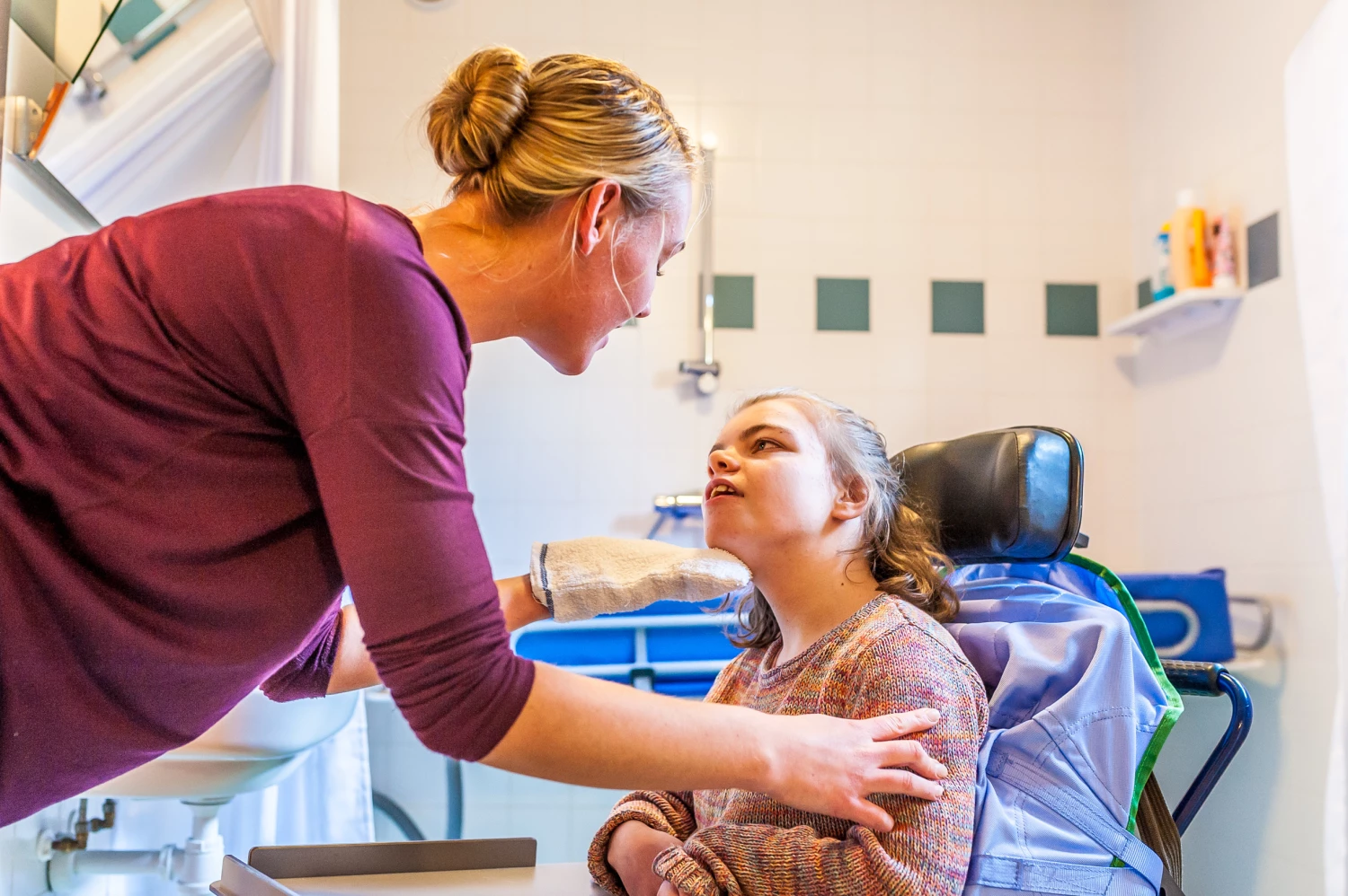 Support worker bathing to a young disabled person in a wheelchair, demonstrating personal care and the varied duties of disability support workers in Australia.