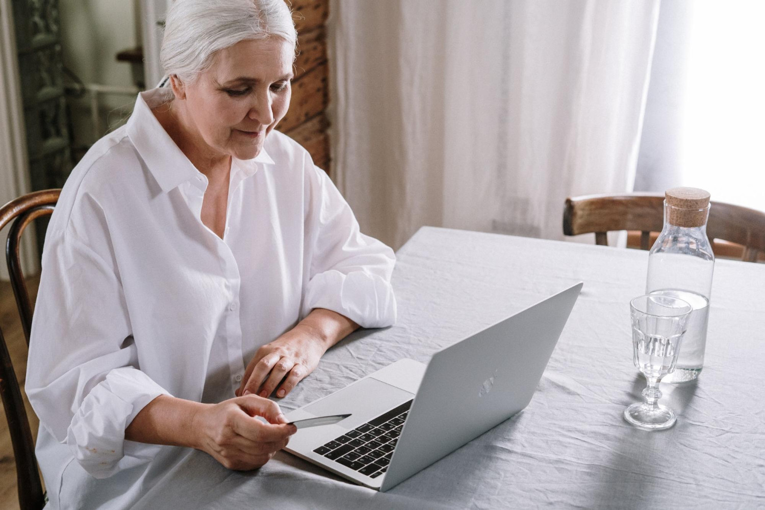 An older woman in white sits at a silver laptop. Focus Care