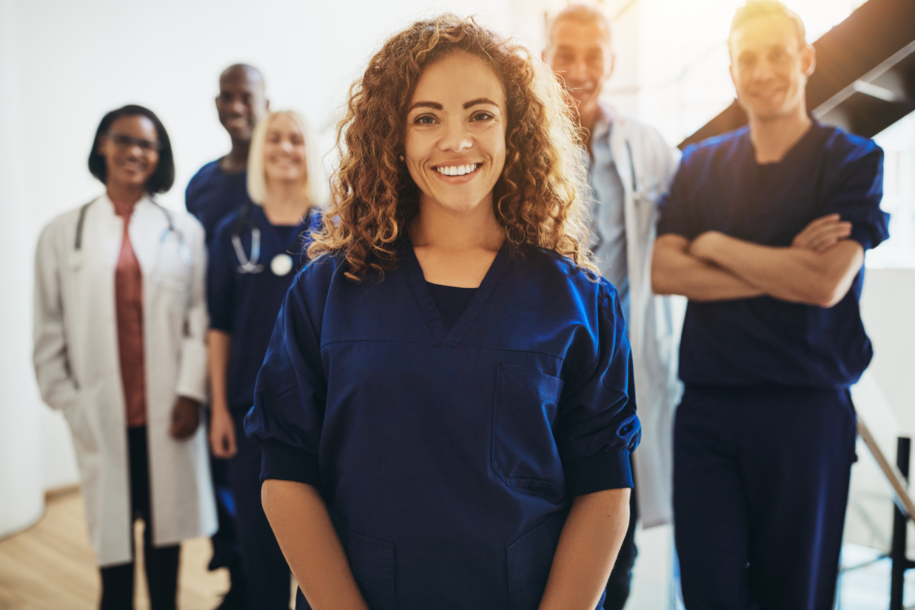 A confident allied health professional stands at the forefront, with a diverse team of healthcare colleagues in the background, representing the broad spectrum of allied health care assistance available to support patient well-being.