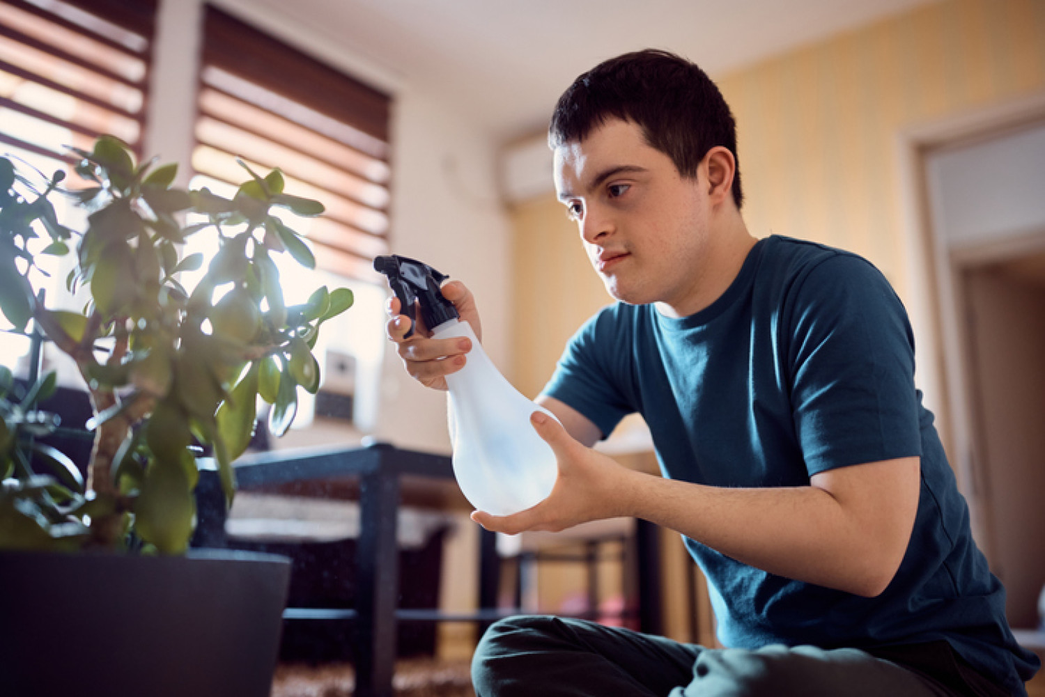 A young man with Down syndrome carefully tending to indoor plants, illustrating the empowerment and daily life skills development supported by NDIS independent living options.
