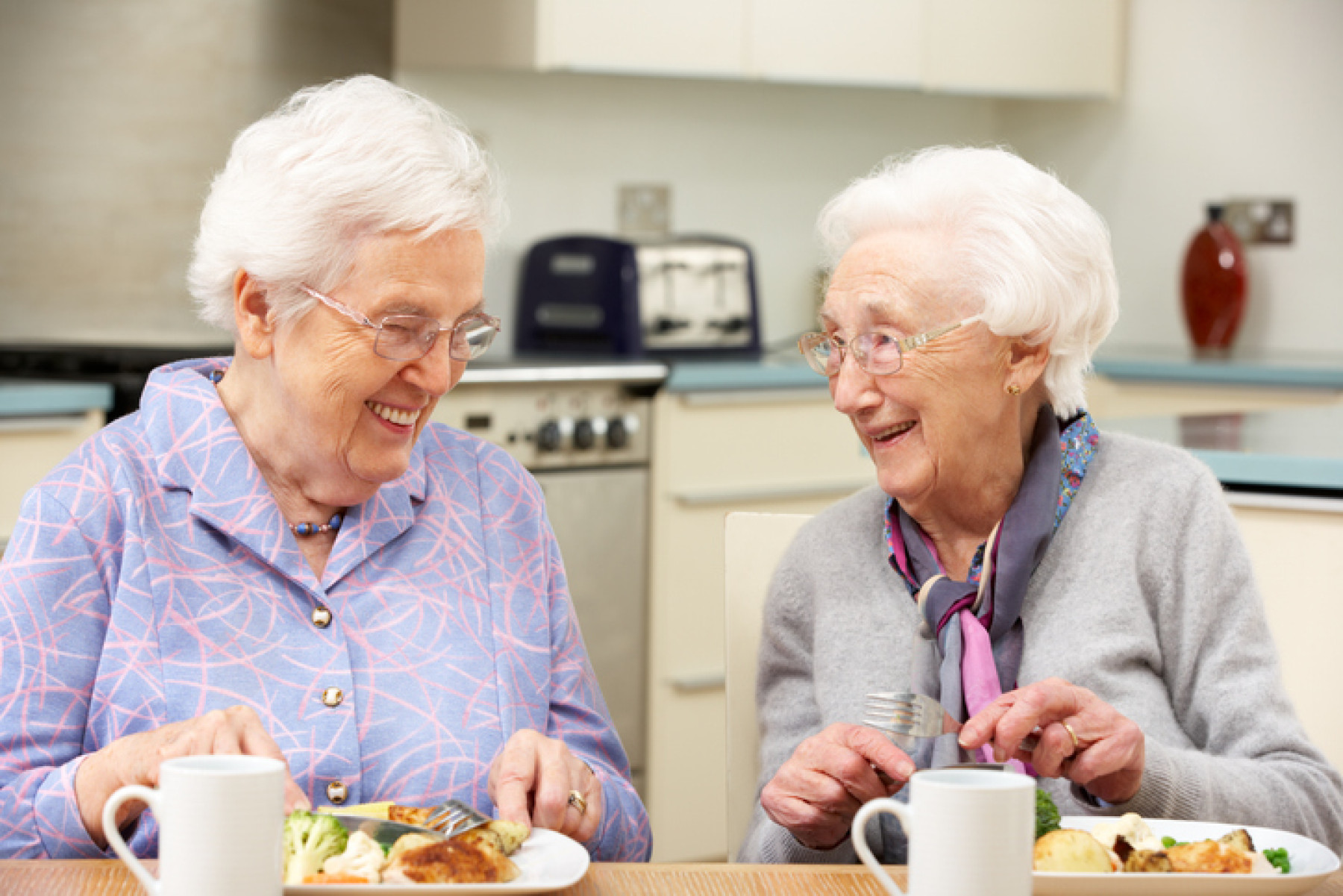 Two elderly women laughing and dining together, representing companionship and the joy of shared independent living under NDIS.