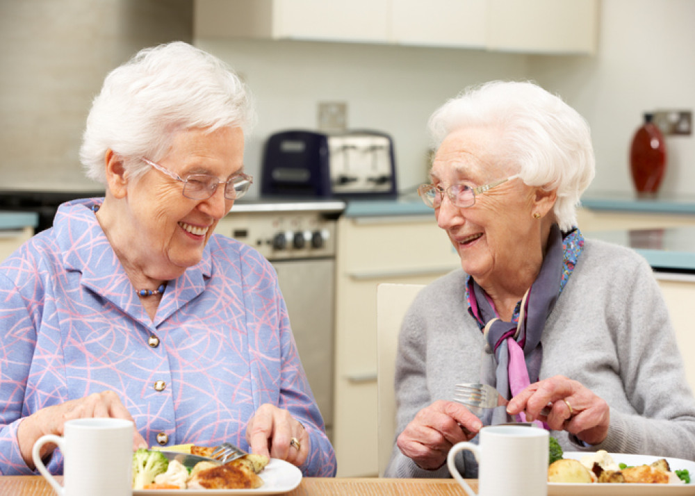 Two elderly women laughing and dining together, representing companionship and the joy of shared independent living under NDIS.