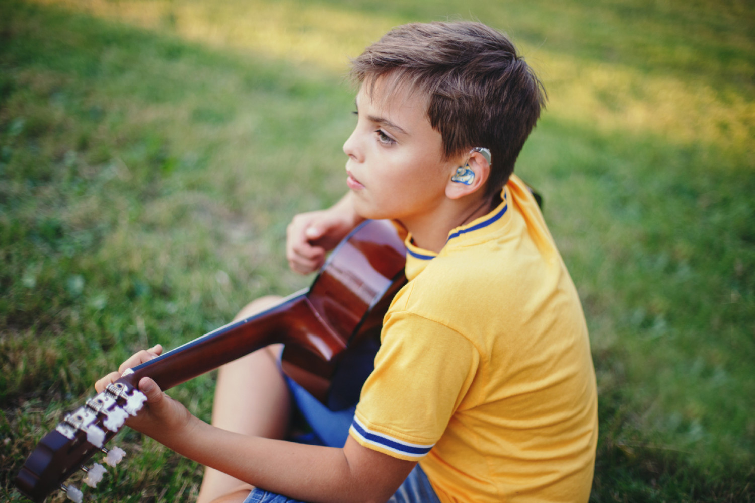 A young student with a hearing aid deeply engaged in playing the guitar, reflecting the empowerment of students with disabilities through Assistive Technology.