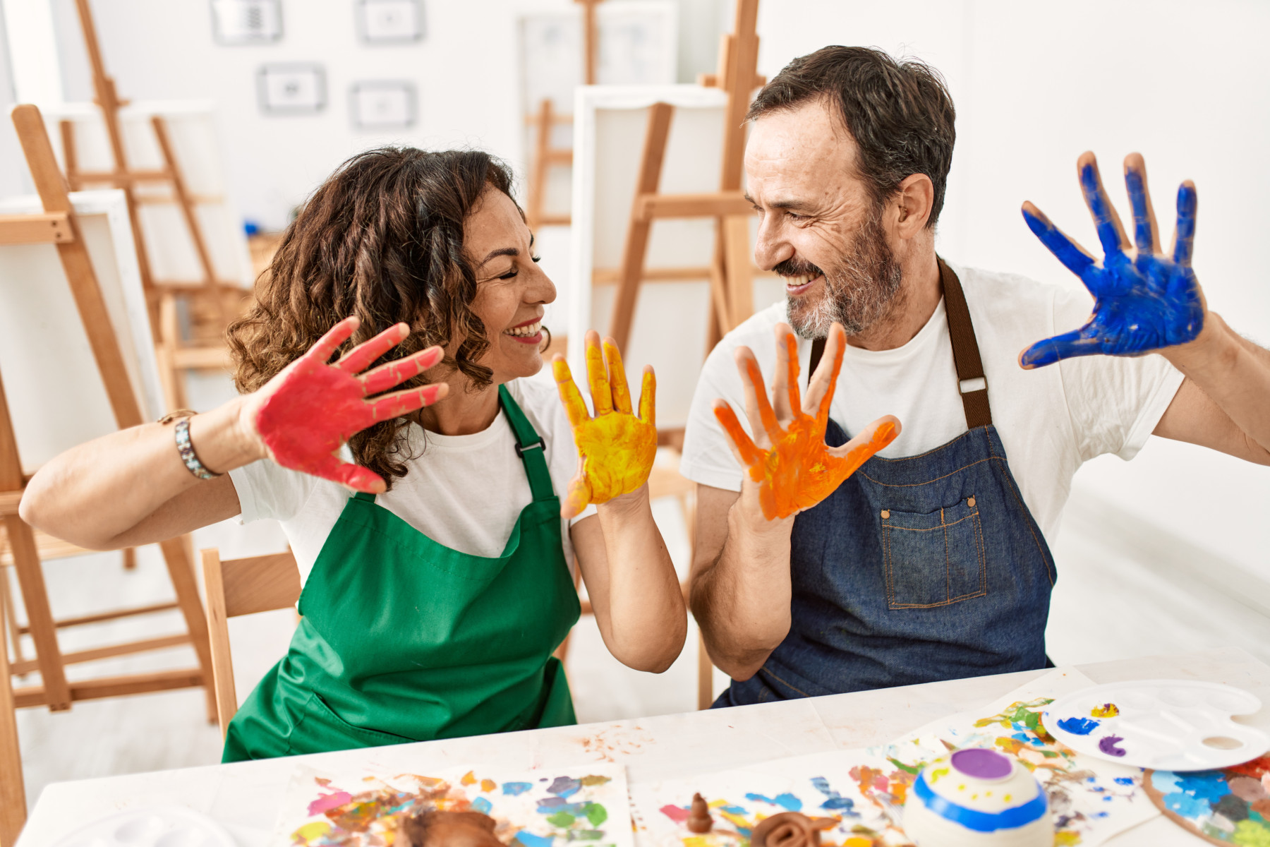 Two adults joyfully showing their paint-covered hands in an disability day programs art therapy class.