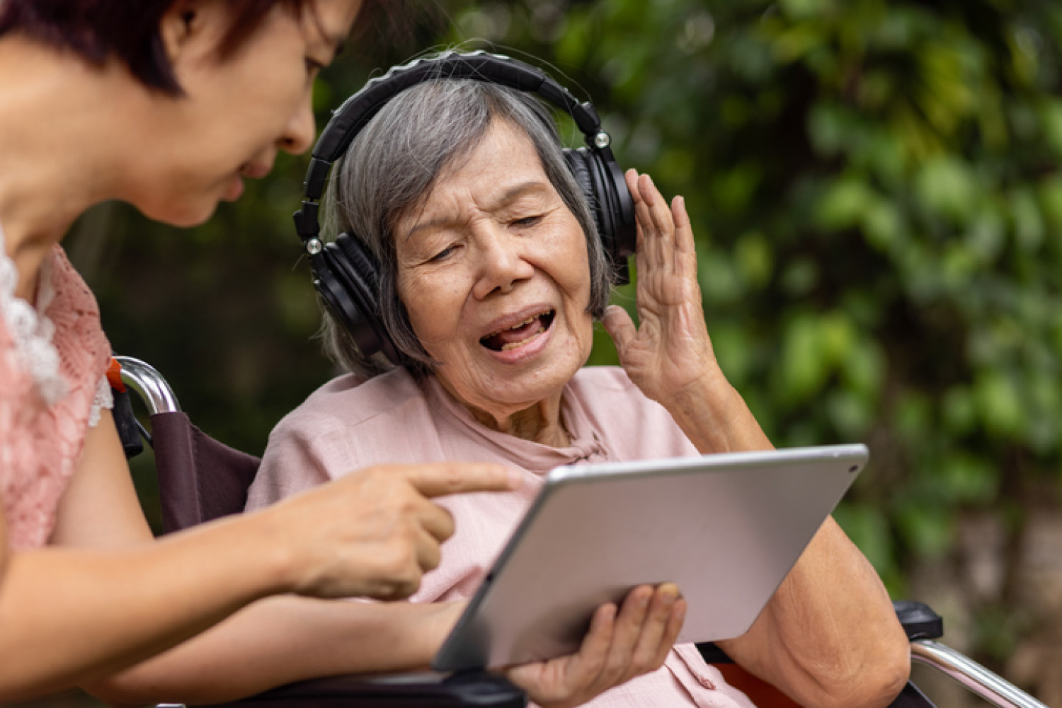 Elderly woman with dementia uses tablet and headphones in music therapy.