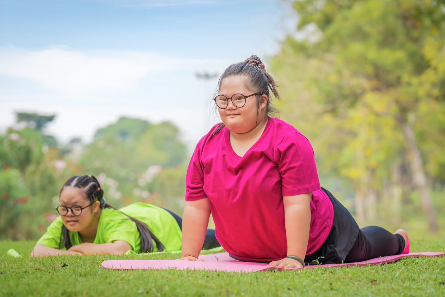 Two young woman with Down syndrome engaging in an outdoor yoga class.
