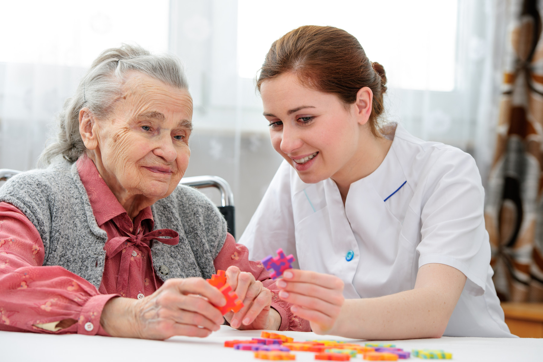 An elderly woman receiving engaging care with a puzzle activity with a care worker, exemplifying the supportive companionship aspect of respite care.