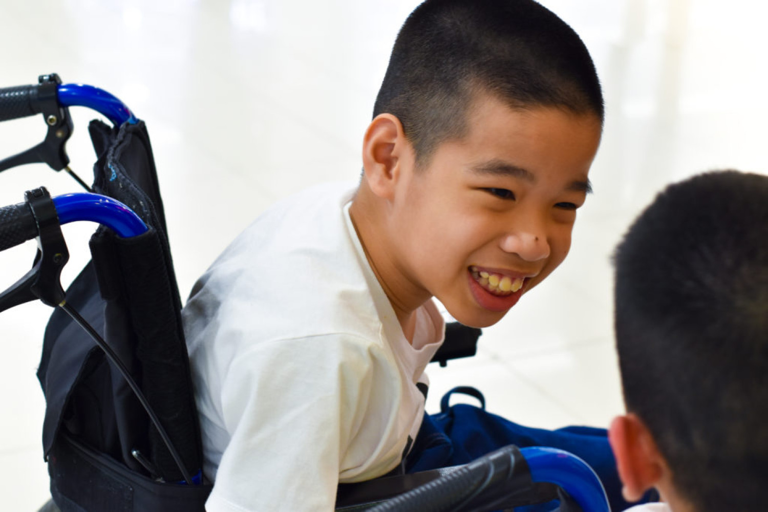 Young Asian boy in wheelchair smiling at friend - Support coordination for people with disabilities - Focus Care.