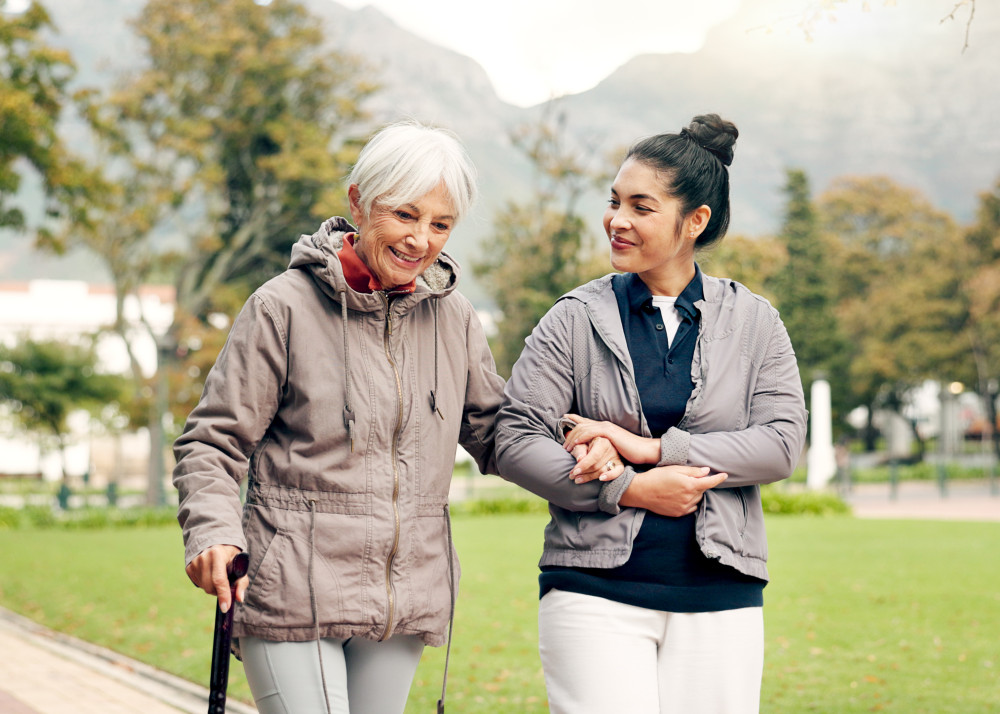Elderly Australian woman being assisted by a support worker on a walk in the park, illustrating the compassionate care in aged support work
